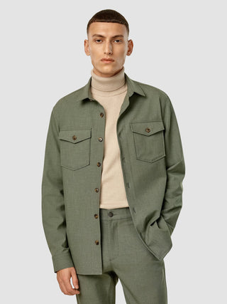 En man bär en beige polotröja under en Essential Overshirt i färgen Nightfall Green Melange tillsammans med matchande byxor.