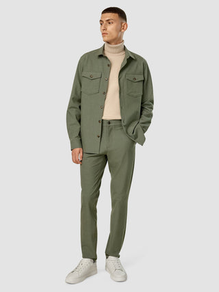 En man klädd i Essential Overshirt Nightfall Green Melange och matchande byxor över en beige polotröja, samt sneakers.