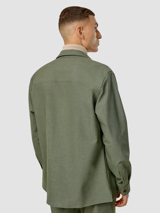 En man sedd bakifrån, klädd i en Essential Overshirt i färgen Nightfall Green Melange över en beige polotröja.