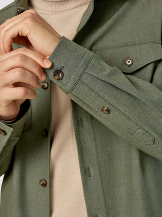 Närbild på en person som justerar den knäppta manschetten på en Essential Overshirt i färgen Nightfall Green Melange över en beige tröja.