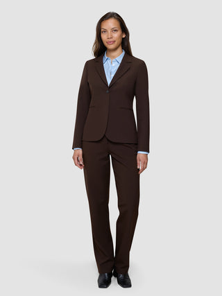 En kvinna klädd i en Women’s Essential Fitted Blazer i färgen Espresso, matchande byxor och en ljusblå skjorta med knappar.