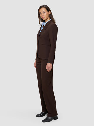 En kvinna klädd i en Women’s Essential Fitted Blazer i färgen Espresso och matchande byxor över en ljusblå skjorta med krage.