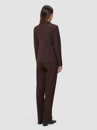 En kvinna sedd bakifrån, klädd i en Women’s Essential Fitted Blazer i färgen Espresso och matchande byxor i skandinavisk design.