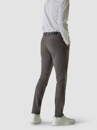 En man sedd bakifrån, klädd i en randig skjorta med knappar, Essential Pants Slim Grey och vita sneakers.