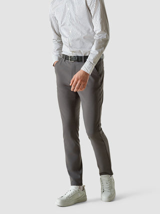 En man i en vit skjorta med tunna ränder och gråa Essential Pants Slim, tillsammans med vita sneakers i skandinavisk design.