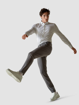En man i en randig skjorta med knappar och ett par gråa Essential Pants Slim mitt i ett steg.