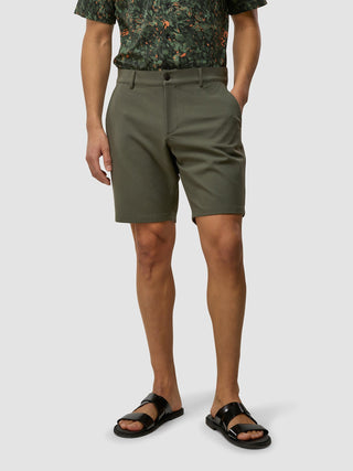 En man klädd i en mönstrad skjorta, GEN2™-shorts i dämpad grön färg och svarta sandaler.