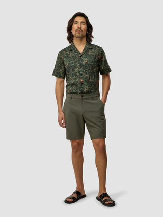 En man i en skjorta med botaniskt mönster, GEN2™-shorts i dämpad grön färg och svarta sandaler.