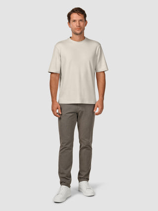 En man klädd i en Heavy Box Fit-T-shirt i färgen Off White, mörka byxor och vita sneakers i en avslappnad skandinavisk stil.