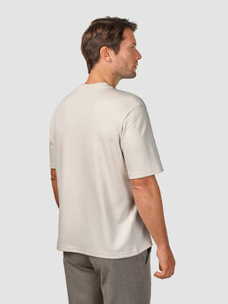 En man sedd bakifrån, klädd i en Heavy Box Fit-T-shirt i färgen Off White och grå byxor.