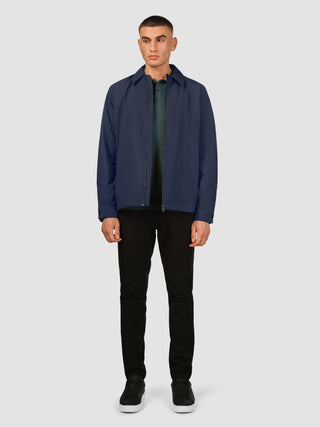 En man klädd i en Hydro Jacket Dark Navy över en grön polotröja, svarta byxor och svarta sneakers.