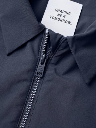 Närbild på en mörk Hydro Jacket i färgen Dark Navy med ett Shaping New Tomorrow-märkesetikett och dragkedjetag.