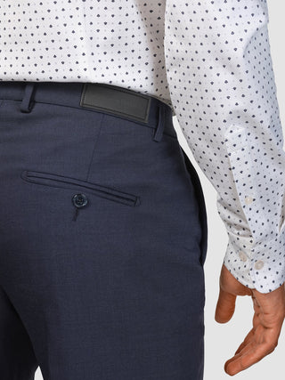 En person i en mönstrad skjorta som är instoppad i Tech Wool Suit Navy-byxor med en märkesetikett i midjan.