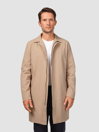 En man klädd i en vattentät trenchcoat i sandfärgat tyg över en vit t-shirt, som speglar den rena skandinaviska designen.