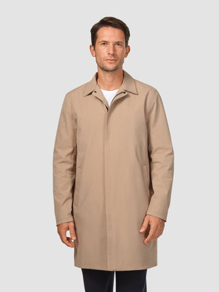 En man klädd i en vattentät trenchcoat i sandfärgat tyg över en vit t-shirt, som präglas av skandinavisk design.