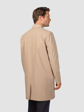 En man sedd bakifrån, klädd i en vattentät trenchcoat i sandfärgat mönster.
