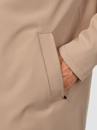 En hand instoppad i sidfickan på en vattentät trenchcoat i sandkornmönster.