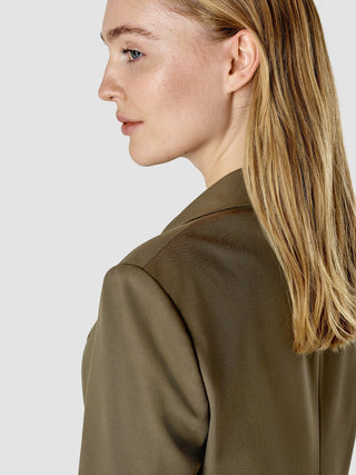 En kvinna i profil som bär en blazer från serien Essential Suit Straight i färgen Dark Olive.