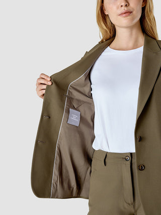 En kvinna klädd i en öppen Essential Suit Straight Dark Olive, där en etikett med texten ”SHAPING NEW TOMORROW” syns.