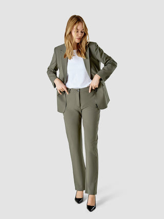 En kvinna klädd i en vit t-shirt och en Essential Suit Straight Dark Olive med matchande byxor.
