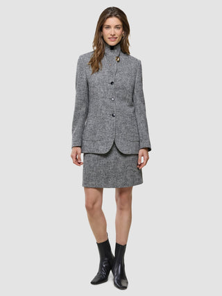 En kvinna bär en grå blazer med svartvitt fiskbensmönster tillsammans med en matchande kort kjol från Women Ashryn och svarta ankelstövlar.