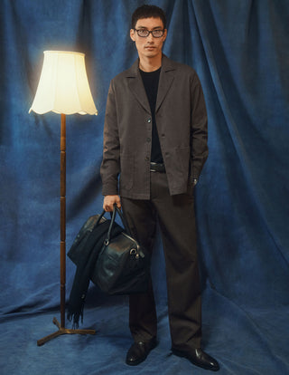 En man klädd i en mörkbeige overshirt från Atelier och matchande byxor, som håller i en svart läderduffelväska.