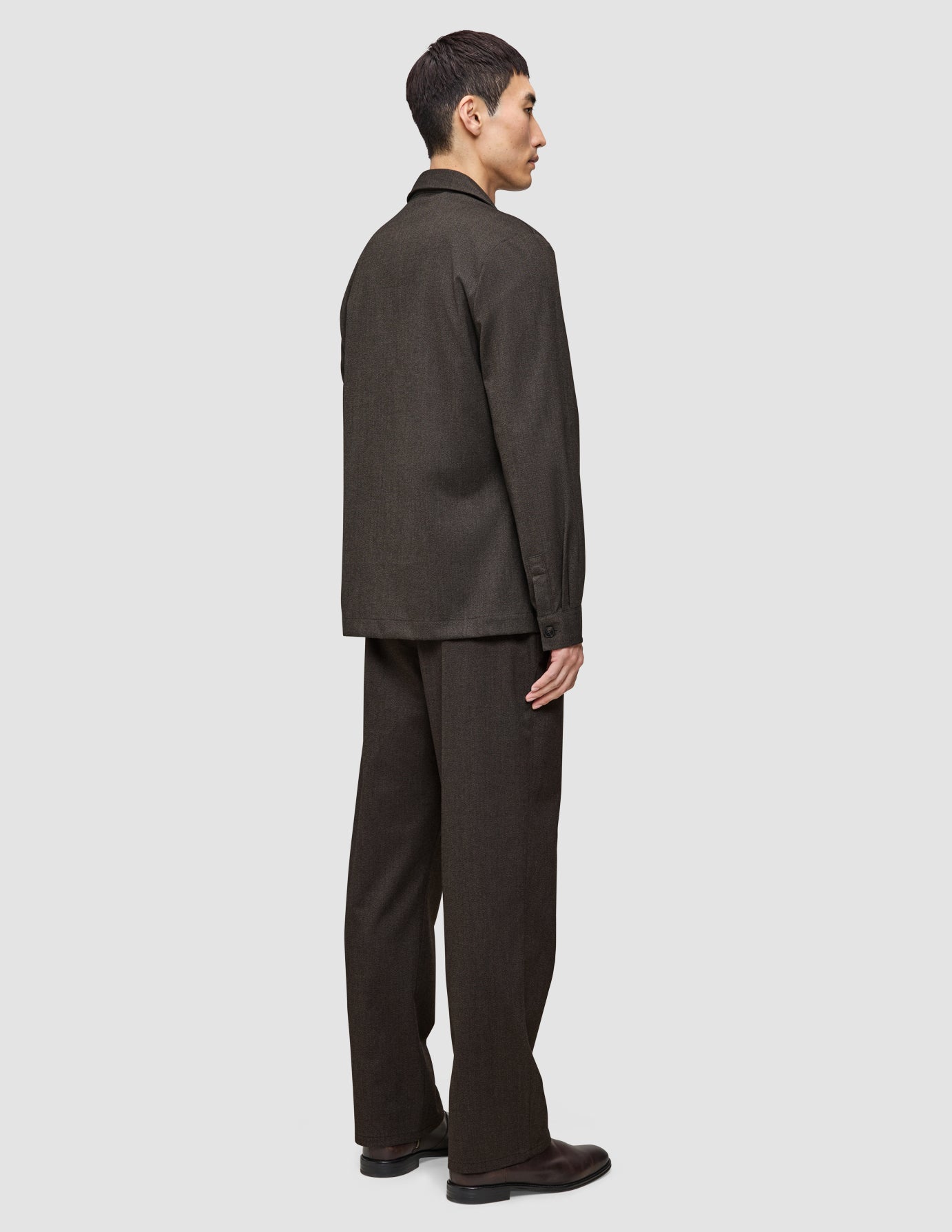 En man sedd från sidan, klädd i en mörkbrun Broken Twill Overshirt från Atelier och matchande byxor.