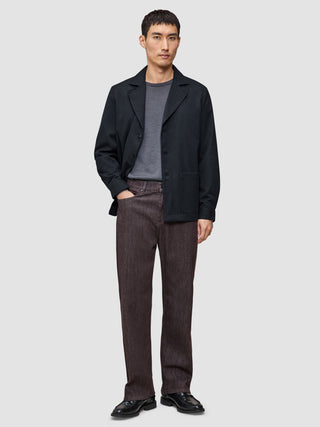 En man klädd i en mörkblå Atelier Overshirt över en grå t-shirt, bruna byxor och svarta loafers.