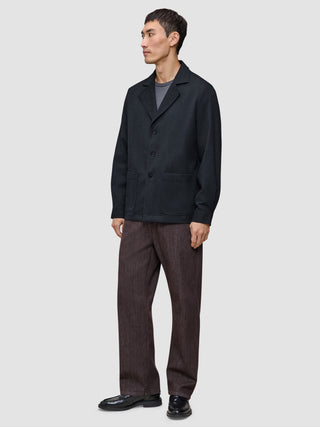En man klädd i en mörkblå Atelier Overshirt, en grå t-shirt och mörka byxor.