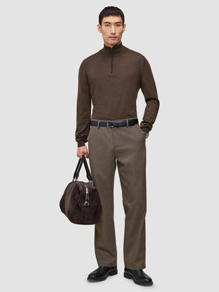 En man klädd i en brun tröja med kvartslång dragkedja och byxor av modellen Atelier Pants Relaxed Dark Beige, som håller i en mörk väska.