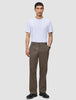 En man i en vit t-shirt, byxor av modellen Atelier Pants Relaxed i mörkbeige och svarta läderskor.