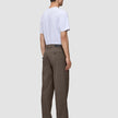 En man sedd bakifrån, klädd i en vit t-shirt och ett par löst sittande byxor i skandinavisk design, Atelier Pants Relaxed Dark Beige.