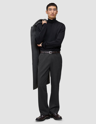 En man i svart polotröja och mörkgråa Atelier Pants Relaxed, med en kappa slängd över axeln i skandinavisk stil.