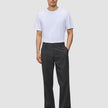En man klädd i en vit t-shirt och byxor av modellen Atelier Pants Relaxed Dark Grey i bruten twill.