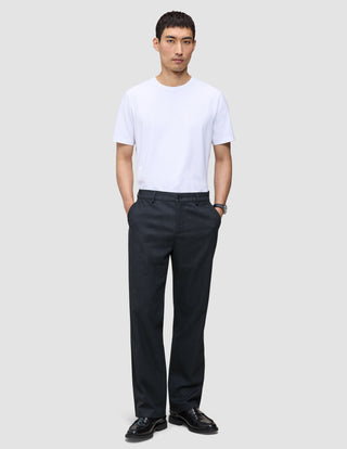 En man bär en vit T-shirt med rund hals och byxor av modellen Atelier Pants Relaxed Dark Navy i bruten twill.