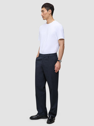 En man klädd i en vit t-shirt och byxor av modellen Atelier Pants Relaxed Dark Navy i bruten twill.