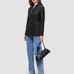 En kvinna klädd i en svart Avira-kavaj för damer i dubbelknäppt modell, tillsammans med blå jeans och en svart axelväska.