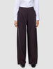 En person bär en vit skjorta med knappar och dambyxorna Avira Pants Wide i färgen Burgundy Berry, som har en avslappnad passform med vida ben.