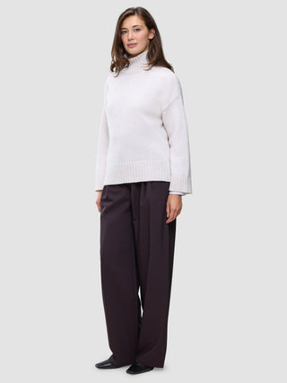 En kvinna klädd i en damtröja av typen Chunky Soft Wool Knit Turtleneck Sugar Melange och mörka byxor med vida ben.