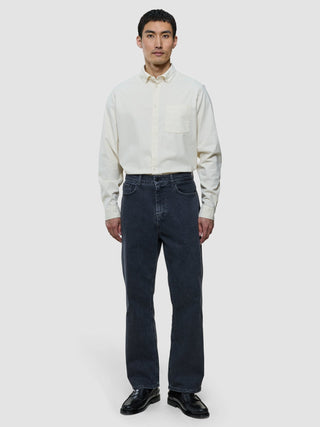 En man klädd i en benvit corduroy-skjorta, mörka jeans och svarta loafers.