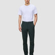 En person klädd i en vit t-shirt, mörkgröna Ease Pants Slim Northern Pine och mörkbruna läderstövlar.