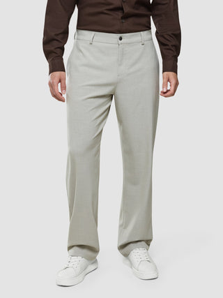 En man klädd i en brun skjorta med knappar och Ease Pants Relaxed Fit Sahara samt vita sneakers.