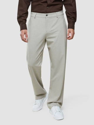 En person klädd i en mörkbrun skjorta med knappar, Ease Pants Relaxed Fit Sahara och vita sneakers.