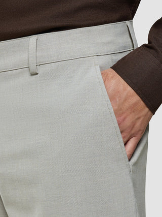En man klädd i en brun skjorta och Ease Pants Relaxed Fit Sahara, med handen i fickan.