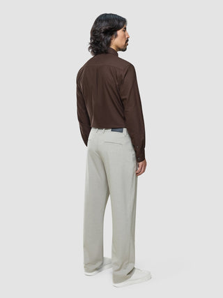 En man sedd bakifrån, klädd i en brun skjorta med knappar, Ease Pants Relaxed Fit Sahara och vita sneakers.
