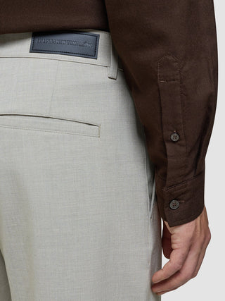 Närbild på de beige Ease Pants Relaxed Fit Sahara med en Shaping New Tomorrow-etikett och en brun långärmad skjorta.