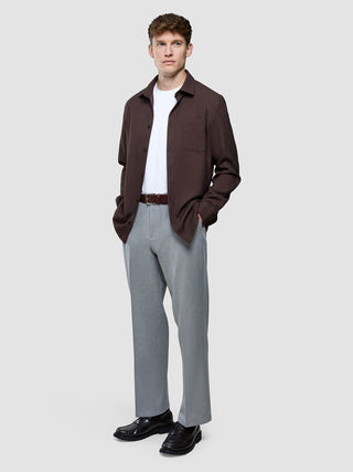 En man klädd i en mörkbrun Effortless-skjorta, en vit t-shirt, grå byxor och svarta loafers.