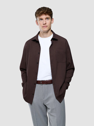 En man bär en mörkbrun Effortless-skjorta över en vit t-shirt och grå byxor.