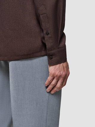 Närbild på en person som bär en Effortless-skjorta samt mörkbruna och grå byxor.