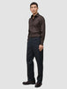 En man klädd i en mörkbrun skjorta av modellen Elevated Shirt Regular, kolgrå byxor och mörka loafers.